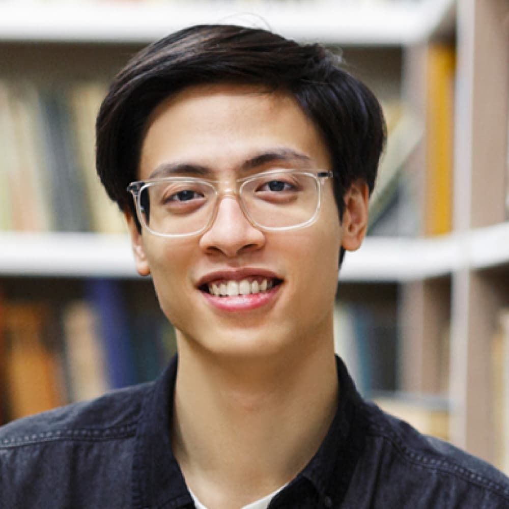 A smiling man with curly hair and confidently. The background features soft, neutral tones, suggesting a warm and welcoming environment.